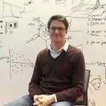 Professor Bill Howe sits in front of a white board with equations and other writing