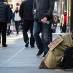 A homeless citizen sits amongst pedestrians.