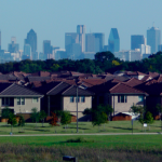 A view of a housing development of single family homes with a dense urban city in the background.