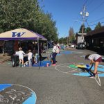 A street with people sitting under a tent and another person drawing in chalk on the road