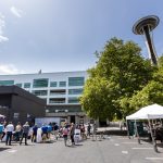 Tents and people gathered around the launch of the delivery hub with the Seattle Space Needle in the back.