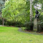 An area of grass lined by a small pathway next to a statue, in Grieg Garden.