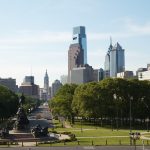 A view of green space surrounding a statue with the Philadelphia skyline in the background.