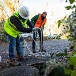 Postdoctoral researcher Raymond RedCorn and research technician John Carter, from left, set-up an autosampler to collect wastewater from a utility hole.