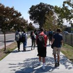 A group of kids walking to school on the sidewalk next to a street