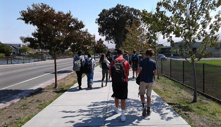 A group of kids walking to school on the sidewalk next to a street