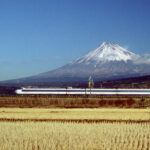 Image of Japanese National Railways 0 series Shinkansen bullet train traveling through countryside running between Mishima and Shinfuji in Japan with Mt. Fuji in background and wheat fields in front