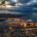 View out an airplane window showing the tail of the plane and a city below at sunset